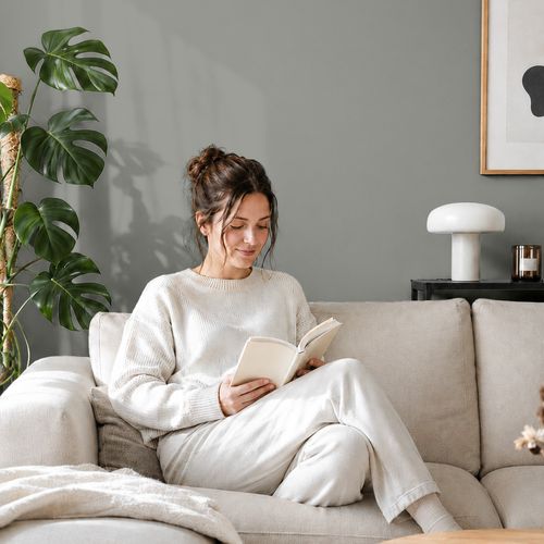 Frau liest ein Buch auf einem Sofa vor einer mit der Farbe "Aschgrau" gestrichenen Wand