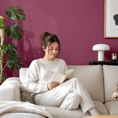 Frau liest ein Buch auf einem Sofa vor einer mit der Farbe "Beerenrot" gestrichenen Wand
