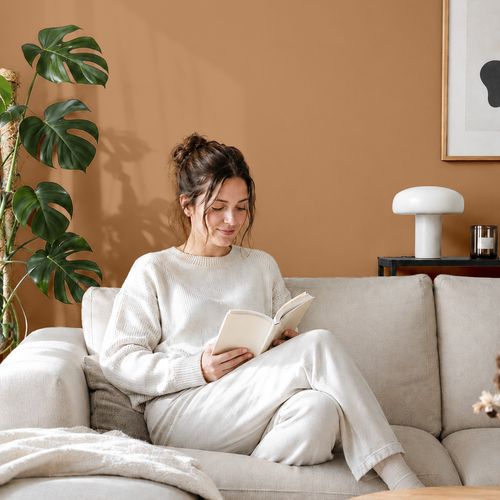 Frau liest ein Buch auf einem Sofa vor einer mit der Farbe "Canyonerde" gestrichenen Wand