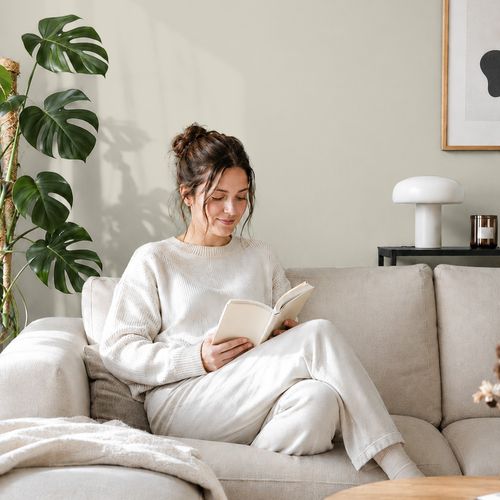 Frau liest ein Buch auf einem Sofa vor einer mit der Farbe "Elfenbeinstrand" gestrichenen Wand