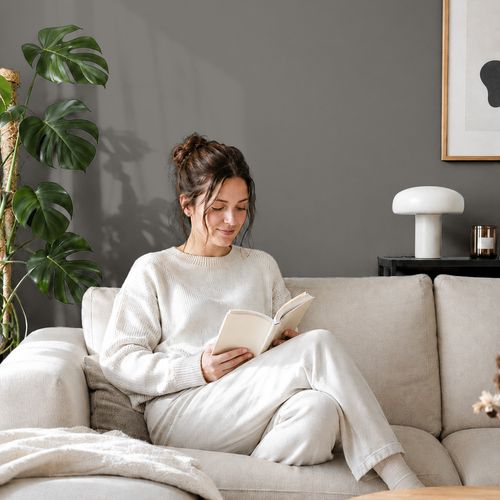 Frau liest ein Buch auf einem Sofa vor einer mit der Farbe "Felsgrau" gestrichenen Wand