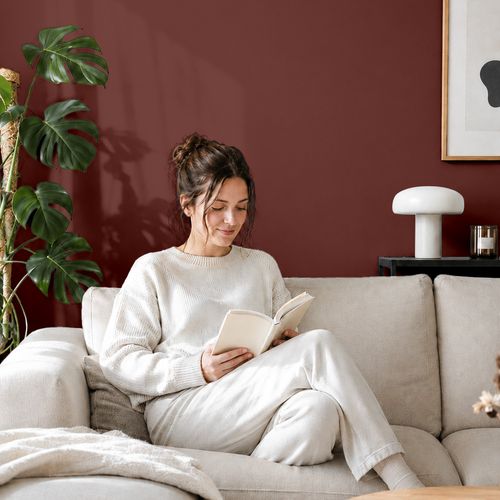 Frau liest ein Buch auf einem Sofa vor einer mit der Farbe "Gewürzorange" gestrichenen Wand