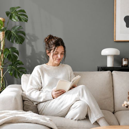 Frau liest ein Buch auf einem Sofa vor einer mit der Farbe "Graphitnebel" gestrichenen Wand