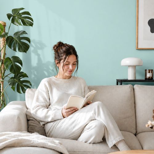 Frau liest ein Buch auf einem Sofa vor einer mit der Farbe "Himmelshauch" gestrichenen Wand