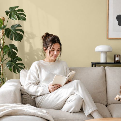 Frau liest ein Buch auf einem Sofa vor einer mit der Farbe "Honigschleier" gestrichenen Wand