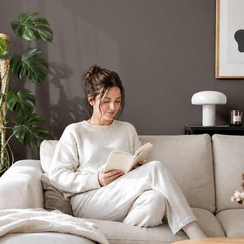 Frau liest ein Buch auf einem Sofa vor einer mit der Farbe "Kohlegrau" gestrichenen Wand