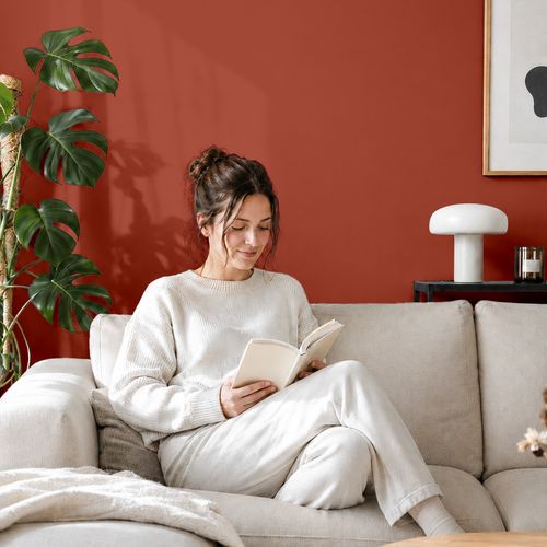 Frau liest ein Buch auf einem Sofa vor einer mit der Farbe "Koralle" gestrichenen Wand