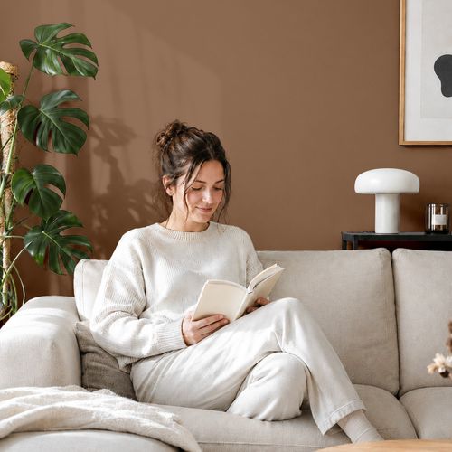Frau liest ein Buch auf einem Sofa vor einer mit der Farbe "Kupferbraun" gestrichenen Wand