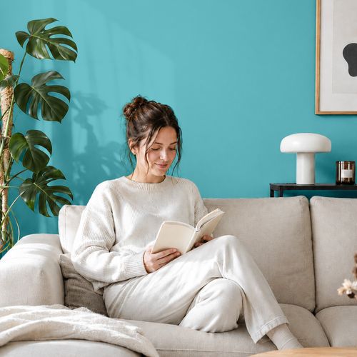 Frau liest ein Buch auf einem Sofa vor einer mit der Farbe "Lagune" gestrichenen Wand