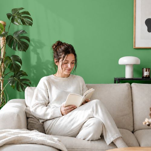 Frau liest ein Buch auf einem Sofa vor einer mit der Farbe "Limettengrün" gestrichenen Wand