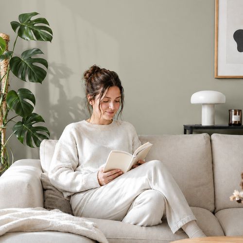 Frau liest ein Buch auf einem Sofa vor einer mit der Farbe "Nebelschwaden" gestrichenen Wand