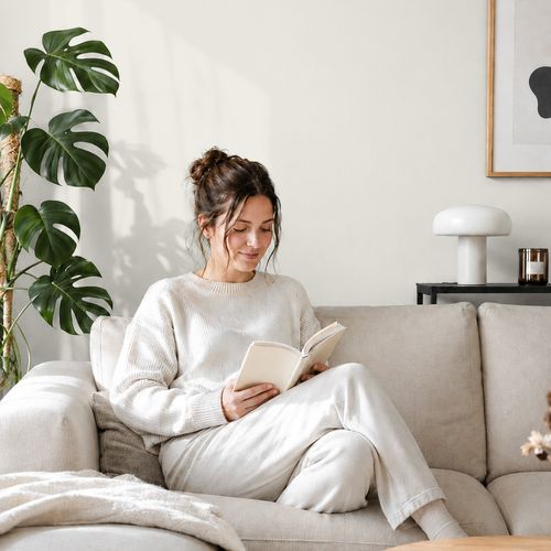 Frau liest ein Buch auf einem Sofa vor einer mit der Farbe "Nordischer Nebel" gestrichenen Wand