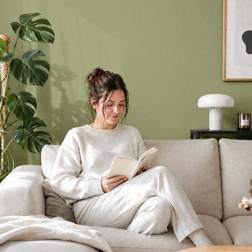 Frau liest ein Buch auf einem Sofa vor einer mit der Farbe "Olivenblatt" gestrichenen Wand