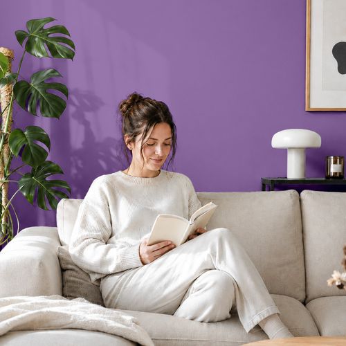 Frau liest ein Buch auf einem Sofa vor einer mit der Farbe "Orchidee" gestrichenen Wand