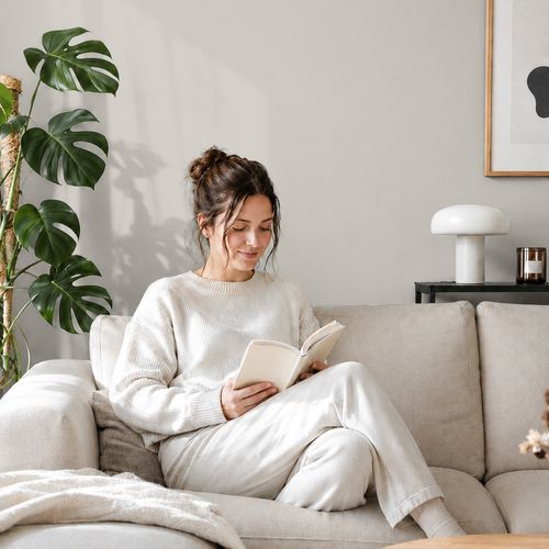 Frau liest ein Buch auf einem Sofa vor einer mit der Farbe "Perlgrau" gestrichenen Wand