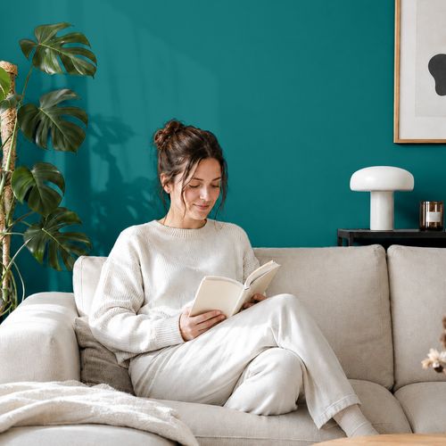 Frau liest ein Buch auf einem Sofa vor einer mit der Farbe "Petrol" gestrichenen Wand