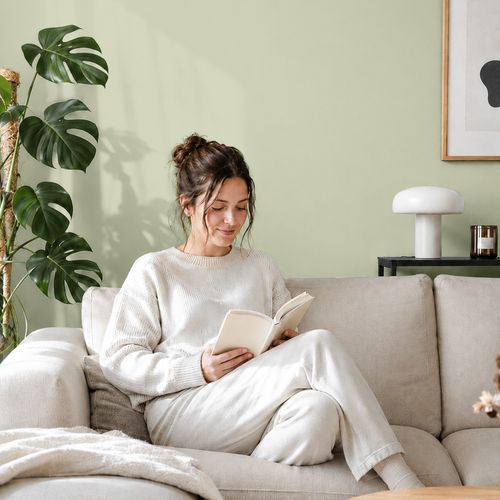 Frau liest ein Buch auf einem Sofa vor einer mit der Farbe "Pistazie" gestrichenen Wand