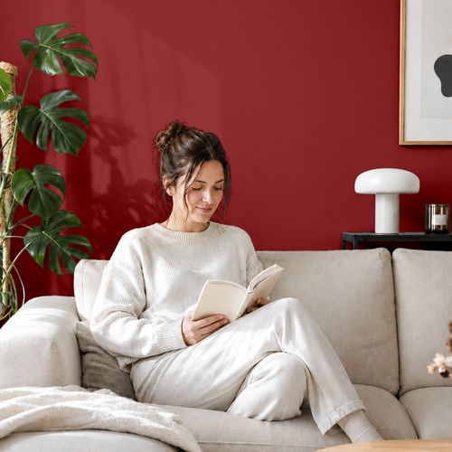 Frau liest ein Buch auf einem Sofa vor einer mit der Farbe "Rubinrot" gestrichenen Wand