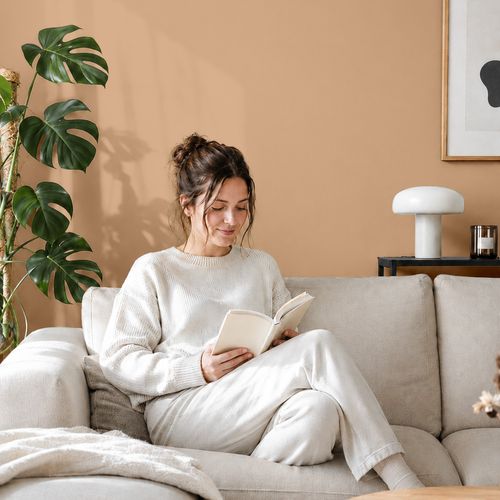 Frau liest ein Buch auf einem Sofa vor einer mit der Farbe "Sanddüne" gestrichenen Wand