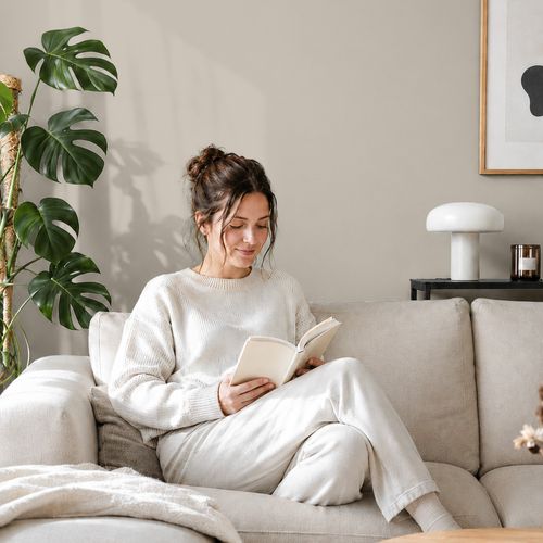 Frau liest ein Buch auf einem Sofa vor einer mit der Farbe "Sanftes Leinen" gestrichenen Wand