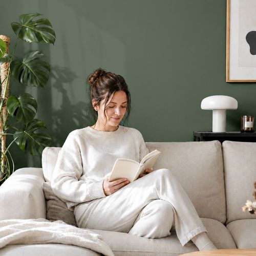 Frau liest ein Buch auf einem Sofa vor einer mit der Farbe "Tannengrün" gestrichenen Wand