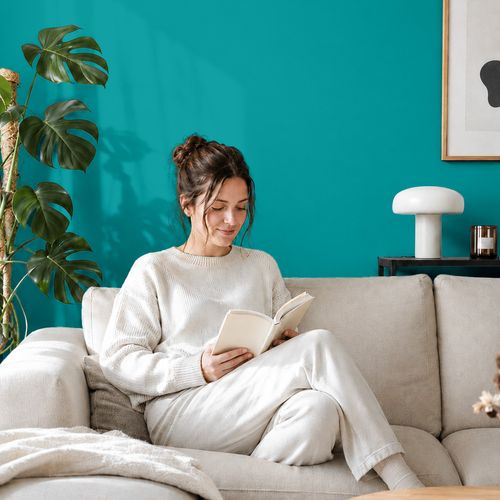 Frau liest ein Buch auf einem Sofa vor einer mit der Farbe "Türkis" gestrichenen Wand