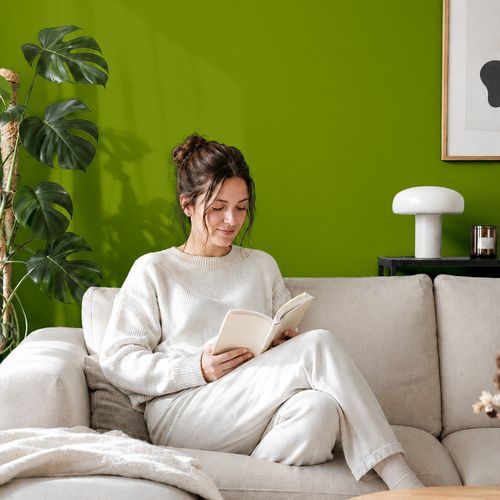 Frau liest ein Buch auf einem Sofa vor einer mit der Farbe "Waldgrün" gestrichenen Wand
