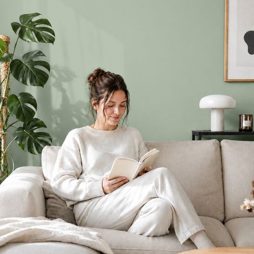 Frau liest ein Buch auf einem Sofa vor einer mit der Farbe "Wiesengrün" gestrichenen Wand