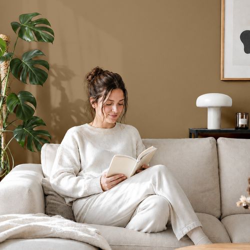 Frau liest ein Buch auf einem Sofa vor einer mit der Farbe "Wüstenpfad" gestrichenen Wand